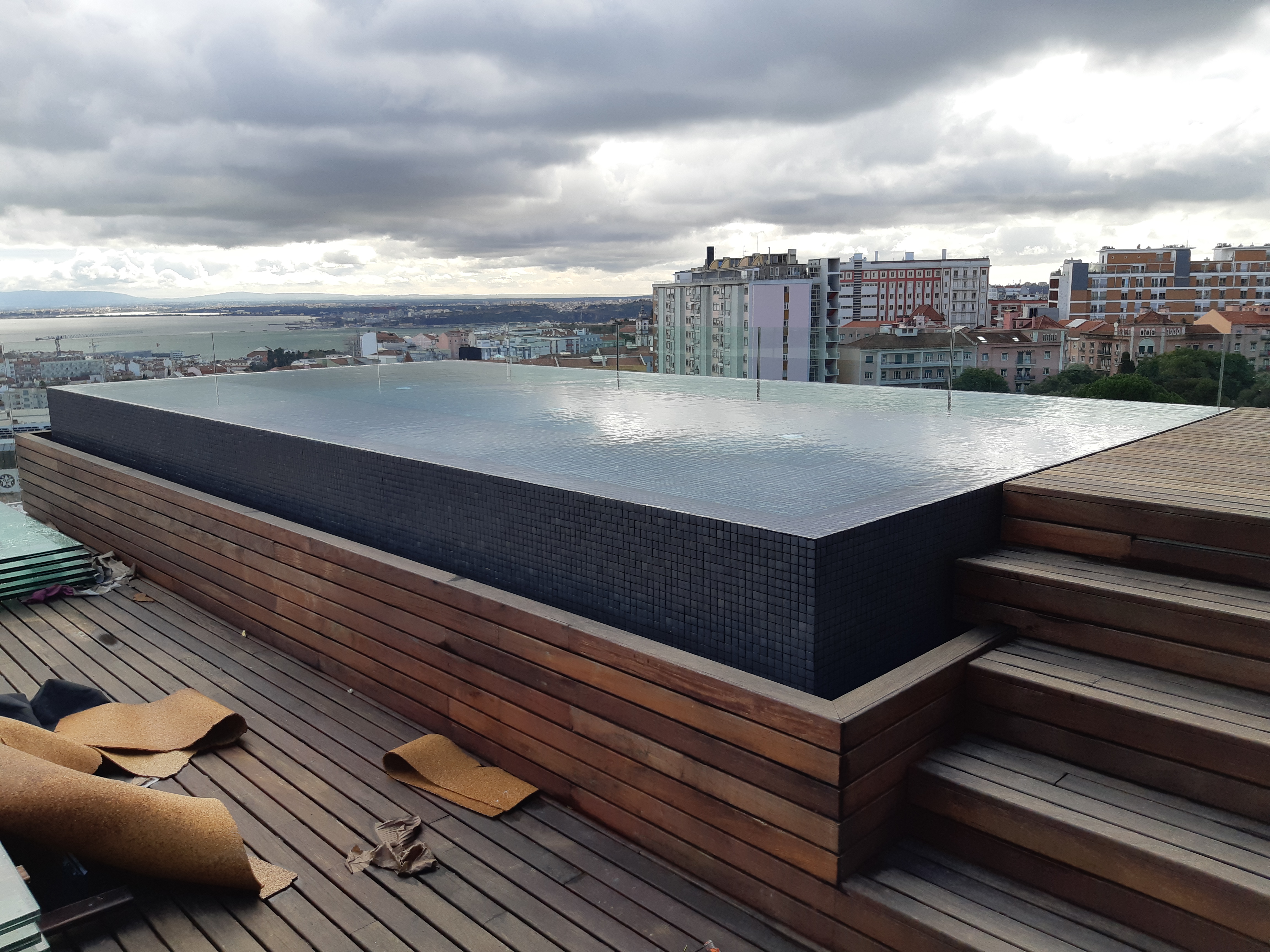 Piscina no topo de um arranha-céus no centro de Lisboa: pastilha preta Hisbalit e junta escura Mapei 114. Transbordo perimetral circular.
